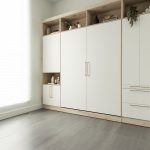 Chambre moderne avec lit escamotable blanc intégré dans un placard en bois, entouré d'étagères avec éclairages encastrés.