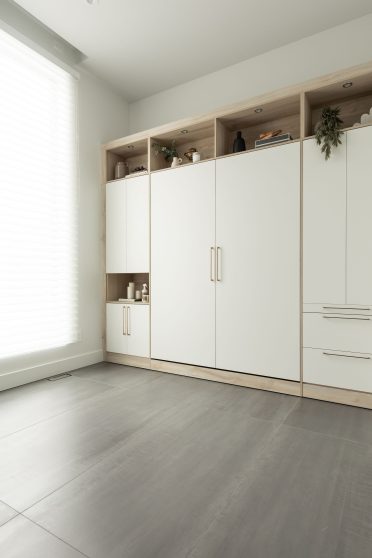 Chambre moderne avec lit escamotable blanc intégré dans un placard en bois, entouré d'étagères avec éclairages encastrés.