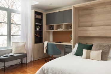 Chambre moderne avec lit escamotable intégré dans un placard en bois, entouré d'étagères et d'un bureau avec éclairages encastrés. 