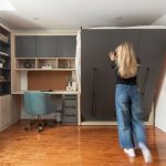 Chambre moderne avec lit escamotable intégré dans un placard en bois, entouré d'étagères et d'un bureau avec éclairages encastrés.