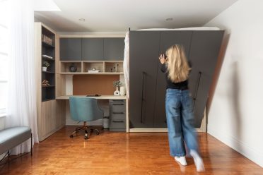 Chambre moderne avec lit escamotable intégré dans un placard en bois, entouré d'étagères et d'un bureau avec éclairages encastrés.