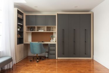 Chambre moderne avec lit escamotable intégré dans un placard en bois, entouré d'étagères et d'un bureau avec éclairages encastrés.