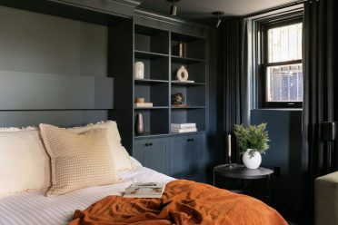 Chambre moderne avec lit escamotable intégré dans un placard en bois bleu, entouré d'étagères. Une couverture orange brûlée donne un effet chaleureux à la pièce.