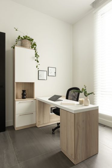 Bureau rétractable déployé dans une pièce lumineuse, avec une femme concentrée devant son ordinateur portable, entourée de rangement sur mesure.
