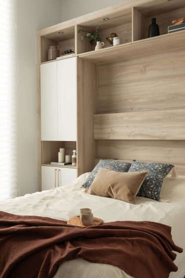 Lit escamotable déployé dans une chambre lumineuse avec rangement en bois clair et objets décoratifs sur les étagères intégrées.