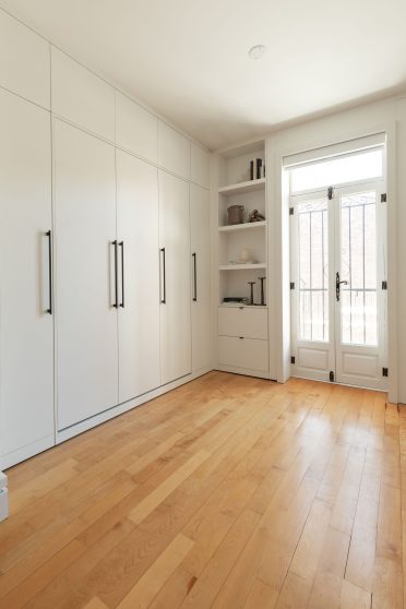 Mobilier fermé tout en blanc dissimulant un lit escamotable Limuro, avec grandes poignées noires et rangements muraux sur mesure.