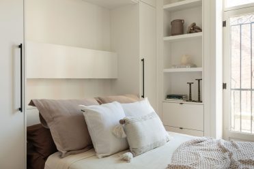 Vue d’ensemble d’une chambre minimaliste avec lit escamotable ouvert, bibliothèques intégrées et portes-fenêtres laissant entrer la lumière naturelle.