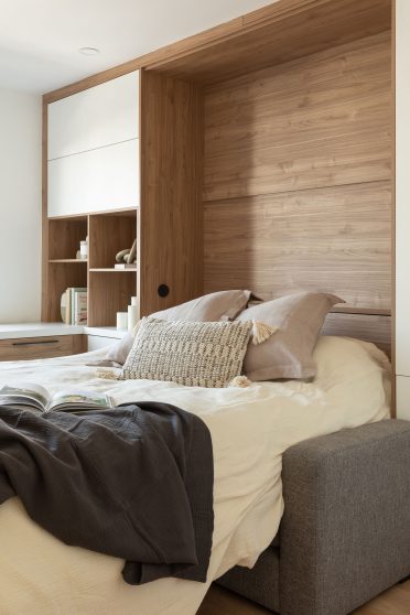 Lit escamotable déployé avec tête de lit en bois et rangement intégré, complété par un sofa gris compact à l’avant.