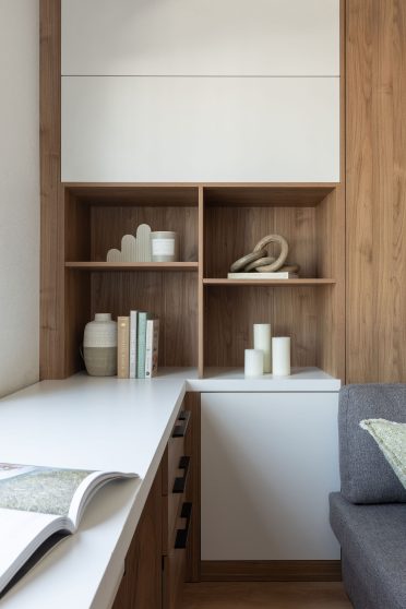 Détail du mobilier sur mesure adjacent au lit escamotable, incluant des étagères ouvertes en bois, un bureau au comptoir blanc et des objets décoratifs soigneusement agencés.