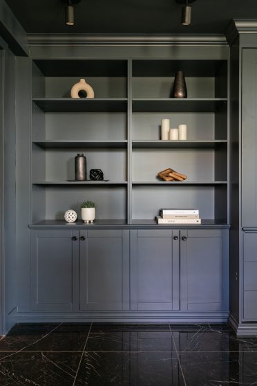 Zoom sur une section de bibliothèque intégrée Oxford, aux lignes sobres et raffinées, décorée d’objets sculpturaux neutres, dans une ambiance feutrée et sophistiquée.