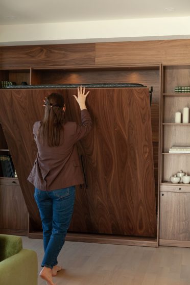 Femme refermant un lit mural escamotable Limuro en bois de noyer. Ce mobilier sur mesure au design raffiné s’intègre harmonieusement dans un intérieur contemporain, combinant esthétisme et fonctionnalité.