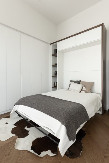 Bureau lumineux aménagé par Limuro avec lit escamotable sur mesure dissimulé dans un meuble mural blanc, rangement intégré et accents de bois foncé, combinant fonctionnalité et design épuré.