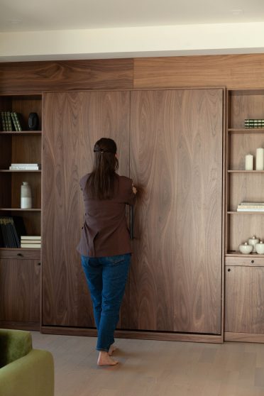 Femme refermant un lit mural escamotable Limuro en bois de noyer. Ce mobilier sur mesure au design raffiné s’intègre harmonieusement dans un intérieur contemporain, combinant esthétisme et fonctionnalité.