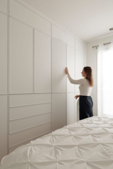 Femme rangeant des vêtements dans un rangement mural sur mesure Limuro, doté de façades blanches minimalistes et d’une niche arrondie intégrée. Un design sobre et pratique qui optimise l’espace de la chambre.