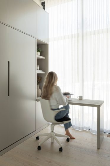 Espace bureau lumineux avec table minimaliste près d’une grande fenêtre, accompagné de rangements intégrés et d’une ambiance épurée.