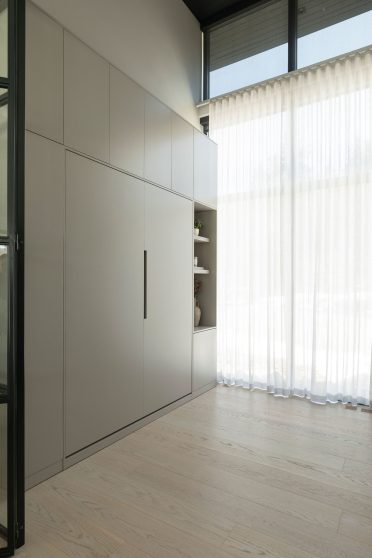 Mur de rangement intégré avec portes minimalistes, baigné de lumière naturelle grâce à une grande fenêtre avec rideaux légers.