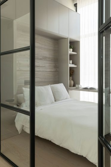 Chambre moderne avec lit intégré, bureau adjacent et cloison vitrée noire, dans un aménagement lumineux et compact.