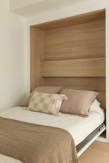 Lit escamotable intégré dans une niche en bois, avec literie aux tons neutres et design épuré.