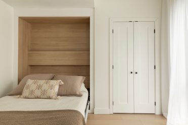 Chambre minimaliste avec lit intégré dans une alcôve en bois, literie aux tons neutres et portes blanches, dans une ambiance douce et épurée.