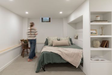 Chambre minimaliste avec lit aux tons verts, rangements intégrés et étagères décoratives, dans un espace lumineux et épuré.