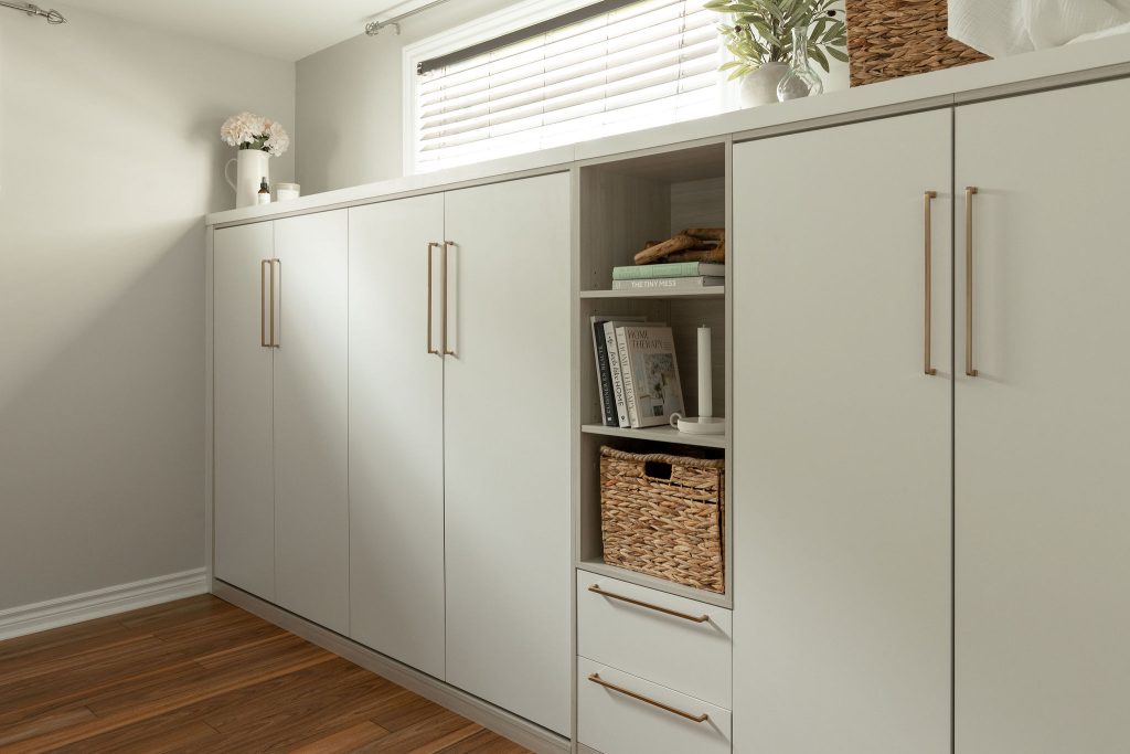 Détail du haut du mobilier intégré : vase en céramique, fleurs et petits objets disposés au-dessus du lit mural replié, dans une chambre au style minimaliste.