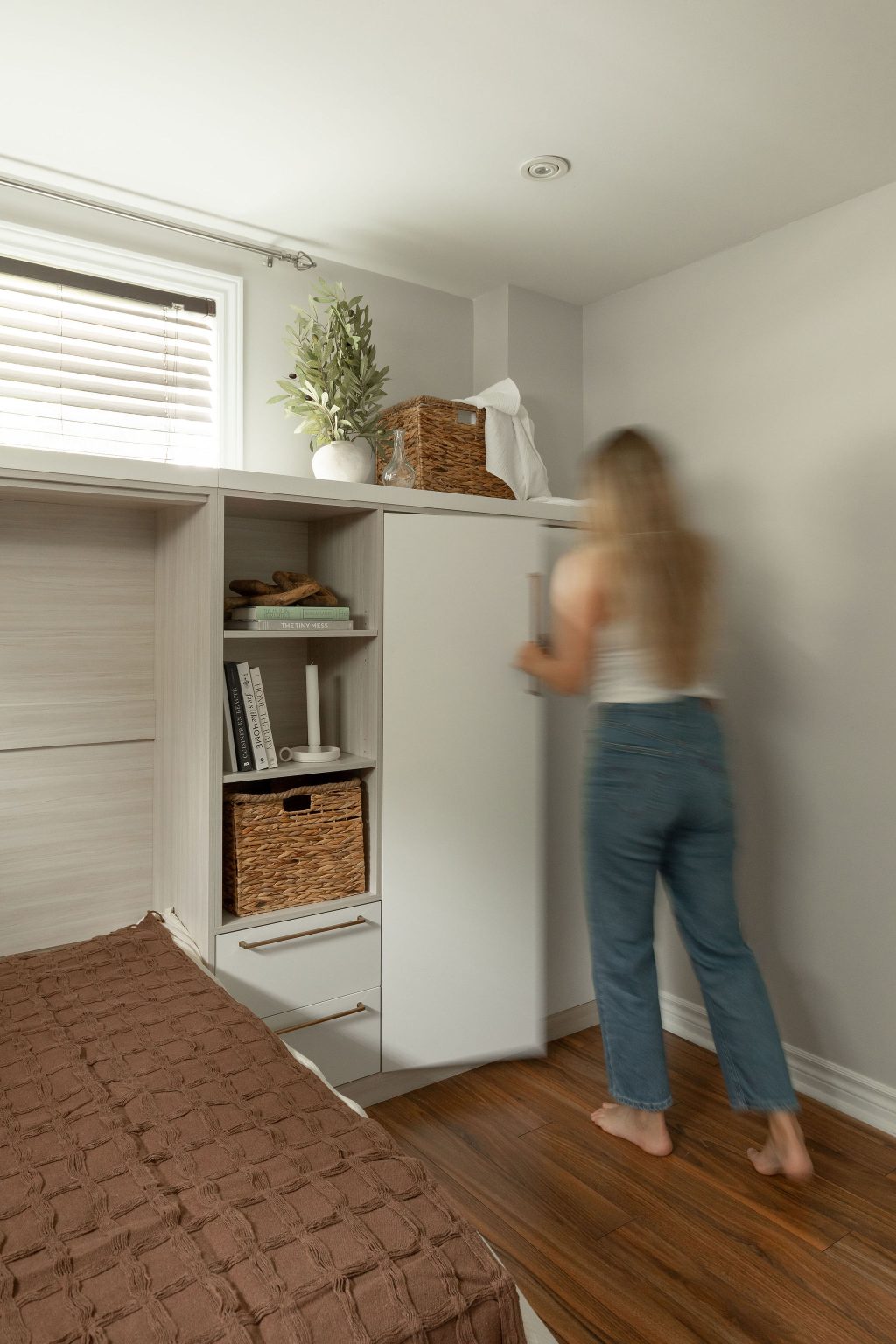 Vue du meuble en situation avec une personne en train d’ouvrir un des panneaux du lit escamotable latéral, illustrant la fonctionnalité fluide du système.