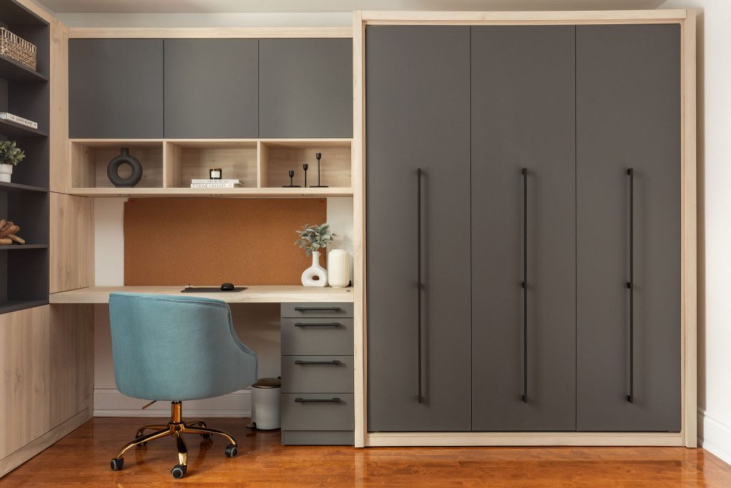 Lit escamotable déployé avec tête de lit en bois clair, intégré à une unité murale comprenant un bureau sur mesure avec rangement, chaise bleue et tablette décorative, dans une chambre au design chaleureux et fonctionnel.