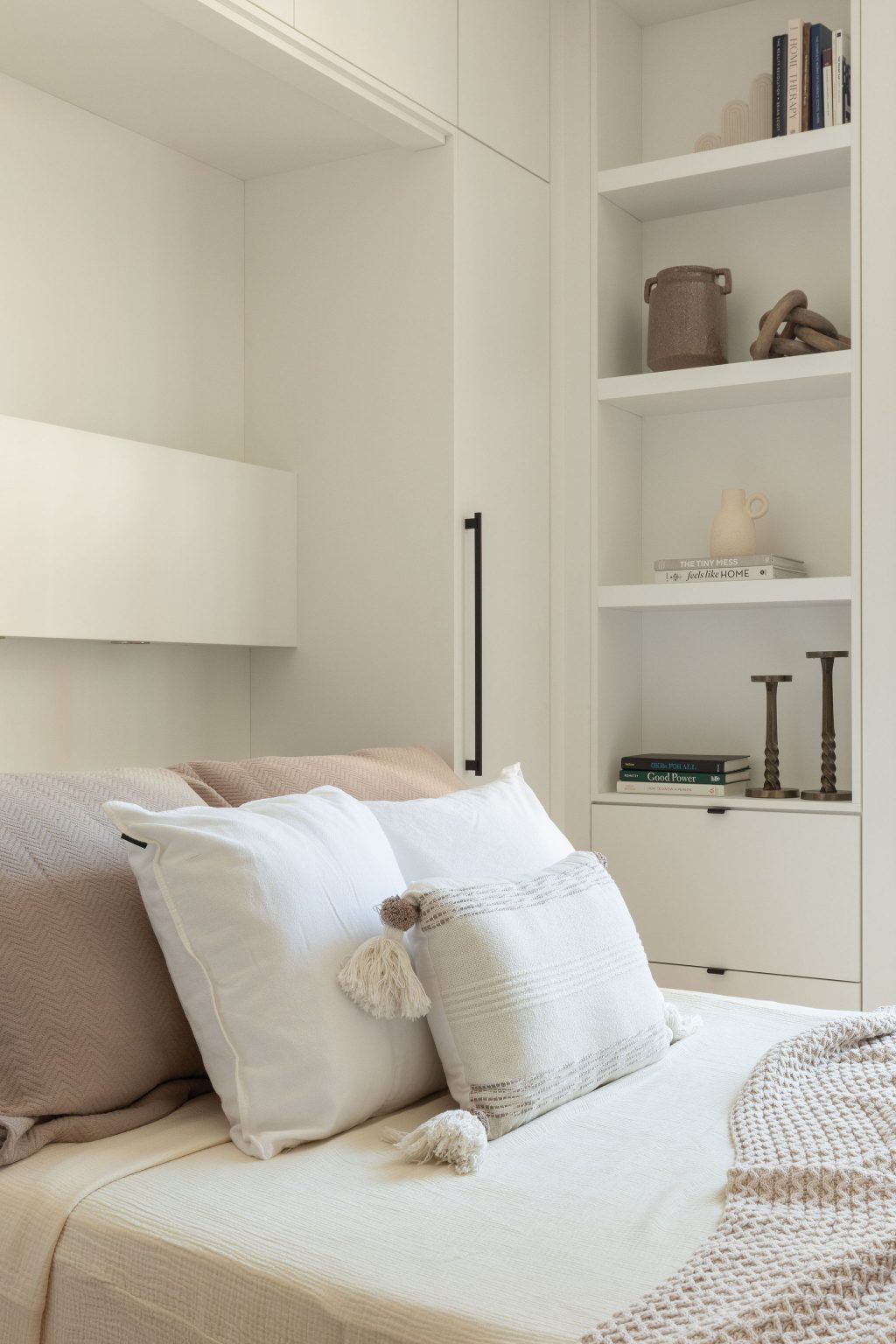 Lit escamotable déployé avec coussins décoratifs et tête de lit blanche, dans une chambre sobre et élégante à l’aménagement intégré Limuro.