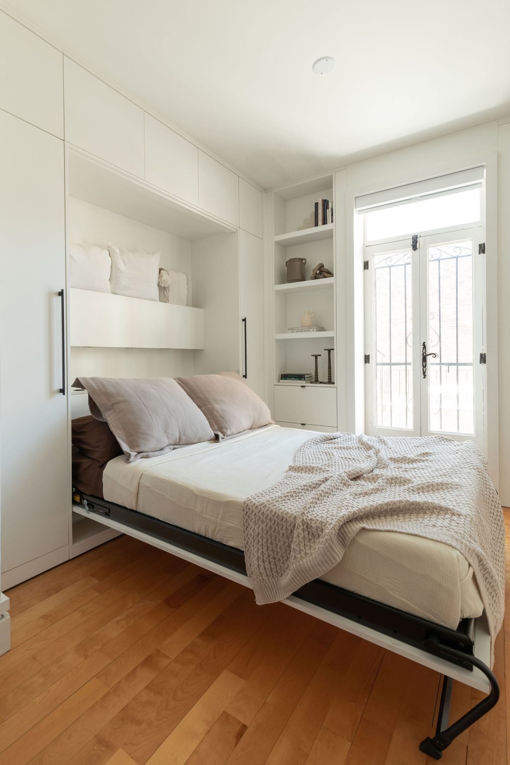 Lit escamotable blanc Limuro déployé dans un loft lumineux avec plancher de bois clair et portes vitrées donnant sur l’extérieur.